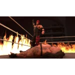 Luchador de pie en un ring en llamas con otro luchador caído Imagen de un luchador de wrestling con ropa negra y roja de pie sobre un ring en llamas con otro luchador caído en el suelo